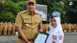 Wali Kota Bekasi Tri Adhianto menyerahkan penghargaan kepada siswi berprestasi, Emily Ravdanty Laras, pada apel pagi Pemkot Bekasi, Senin (15/9/2025).