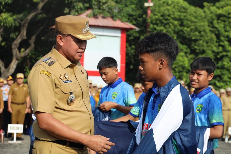 Wali Kota Bekasi Tri Adhianto menyerahkan atribut kepada salah satu pemain Tim Tajimalela yang akan berlaga di Turnamen Internasional Singa Cup U-14 di Singapura. Pelepasan tim dilakukan di Plaza Pemerintah Kota Bekasi, Senin (27/10/2025). (Foto: Diskominfostandi Kota Bekasi)