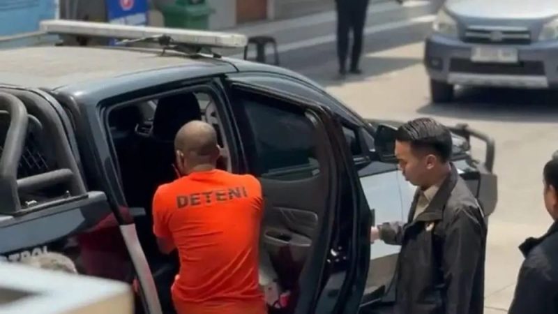 Petugas mengawal seorang warga negara Nigeria berinisial OCO yang mengenakan pakaian bertuliskan “DETENI” saat hendak dimasukkan ke dalam kendaraan. OCO ditetapkan sebagai tersangka dugaan tindak pidana keimigrasian setelah tercatat overstay selama 3.073 hari atau lebih dari delapan tahun.