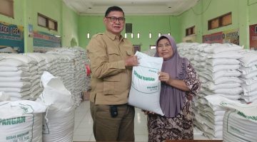 Kepala Desa Muktiwari, Bahrudin, SE, secara simbolis menyerahkan bantuan pangan berupa beras medium 10 kilogram kepada salah satu Keluarga Penerima Manfaat (KPM) di Aula Desa Muktiwari, Kecamatan Cibitung, Kabupaten Bekasi, Senin (24/8/2026). Sebanyak 1.902 KPM menerima bantuan 30 kilogram beras per KK melalui Program Bantuan Pangan Pemerintah Pusat yang disalurkan oleh Perum Bulog.