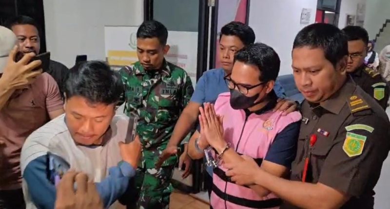 Tersangka AEZ mengenakan rompi tahanan berwarna pink dan dikawal petugas Kejaksaan Negeri Kabupaten Bekasi saat keluar usai menjalani pemeriksaan, Senin (10/8/2026). AEZ kemudian dibawa ke Lapas Kelas IIA Cikarang untuk menjalani penahanan selama 20 hari dalam perkara dugaan korupsi sambungan langganan Perumda Tirta Bhagasasi.