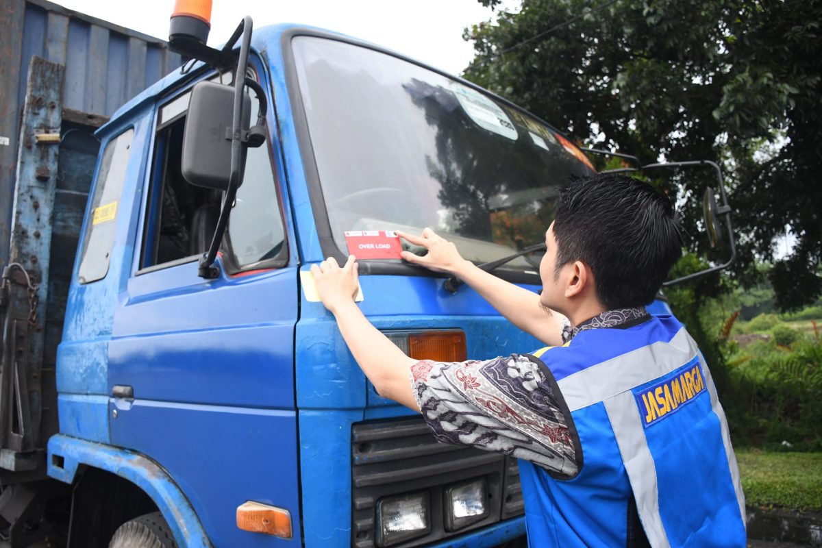 Petugas Jasamarga menempelkan stiker peringatan "Over Load" pada kendaraan angkutan barang yang terindikasi melebihi batas muatan dalam kegiatan penertiban Over Dimension Over Load (ODOL) di ruas tol sebagai bagian dari dukungan menuju target Zero ODOL 2027.