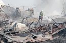 Petugas pemadam kebakaran melakukan pendinginan di lokasi kebakaran. Sejumlah bangunan dan material tampak hangus terbakar, sementara asap masih mengepul di area kejadian.
