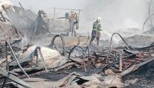 Petugas pemadam kebakaran melakukan pendinginan di lokasi kebakaran. Sejumlah bangunan dan material tampak hangus terbakar, sementara asap masih mengepul di area kejadian.