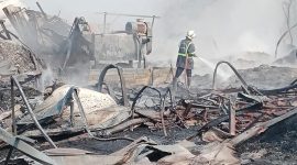 Petugas pemadam kebakaran melakukan pendinginan di lokasi kebakaran. Sejumlah bangunan dan material tampak hangus terbakar, sementara asap masih mengepul di area kejadian.