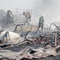 Petugas pemadam kebakaran melakukan pendinginan di lokasi kebakaran. Sejumlah bangunan dan material tampak hangus terbakar, sementara asap masih mengepul di area kejadian.